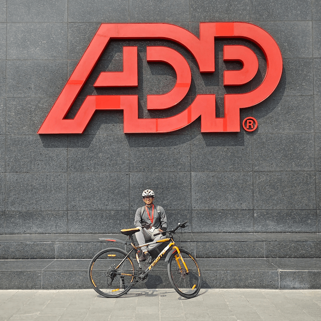 Me posing proudly with my bike in front of a large, red ADP corporate sign at the office entrance.
