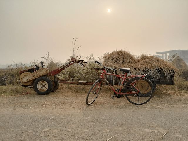 A vintage, single-speed bicycle in front of a tractor in the outskirts.